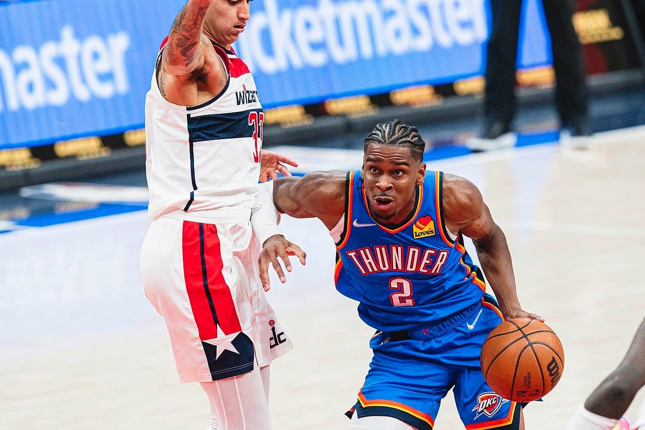 Shai Gilgeous-Alexander in a blue Oklahoma City Thunder number 2 jersey drives with the ball past a Washington Wizards defender