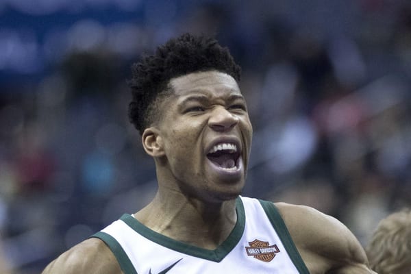 Giannis Antetokounmpo in a white Milwaukee Bucks jersey shouts with his mouth wide open before a game