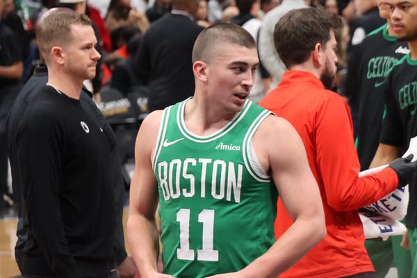 Payton Pritchard in a green Boston Celtics jersey, number 11, stands at the bench among coaches and staff during a game