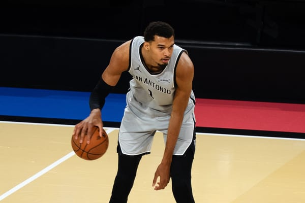 Victor Wembanyama in a grey San Antonio Spurs jersey crouches low and dribbles the ball with his right hand