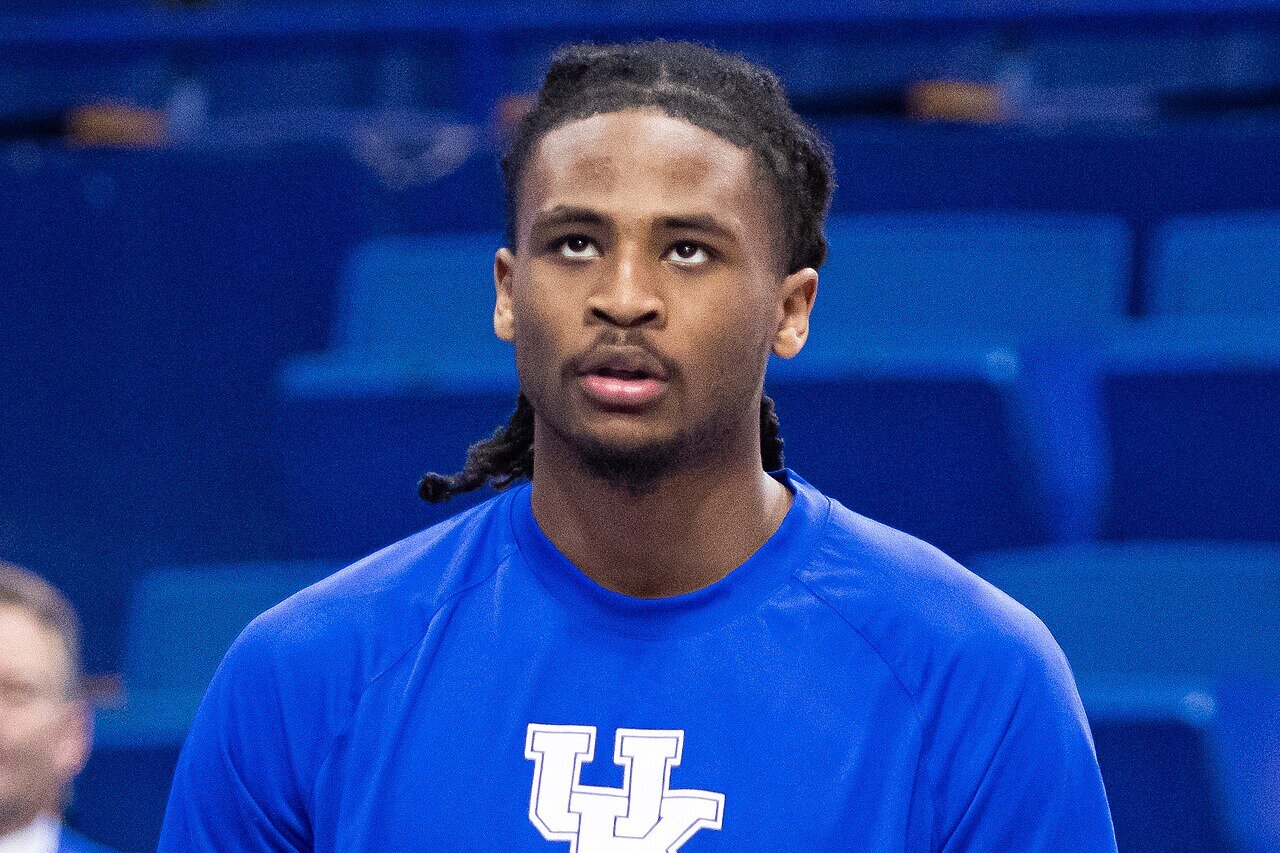 Cason Wallace in a blue Kentucky shirt holds a basketball in both hands during pregame warmups in an arena with empty seats behind him