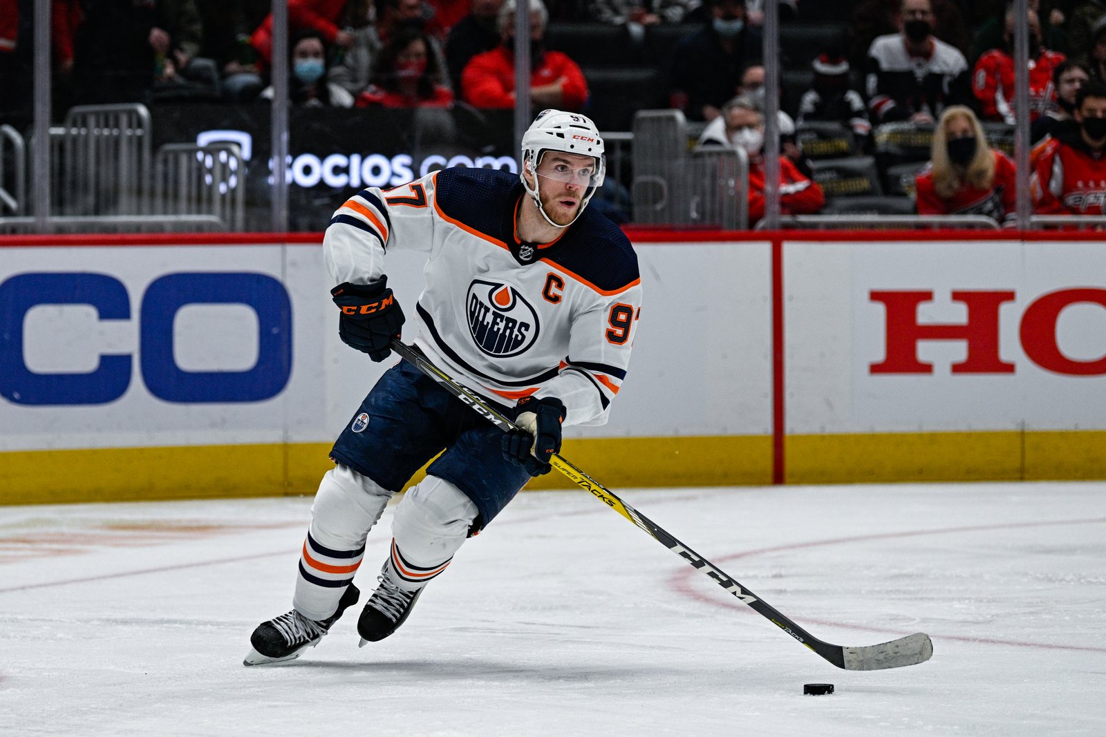 Connor McDavid in a white Edmonton Oilers road jersey with the captain's C skates with the puck in front of the boards