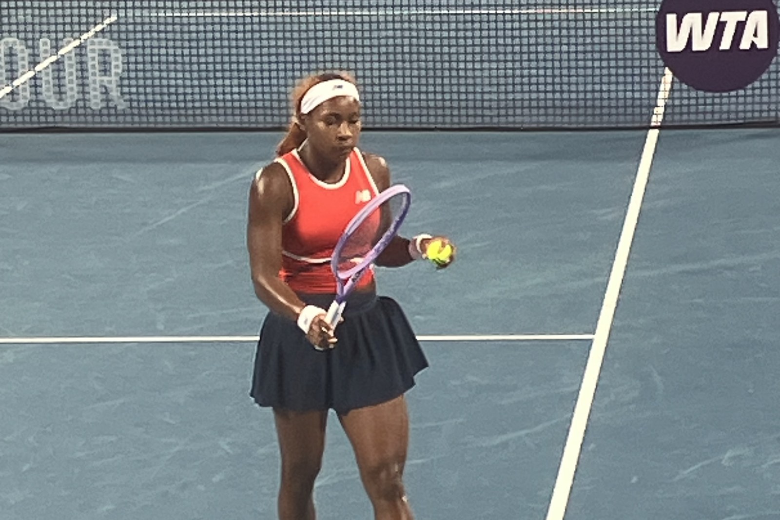 Coco Gauff preparing to serve, racquet and ball raised, on a blue hard court