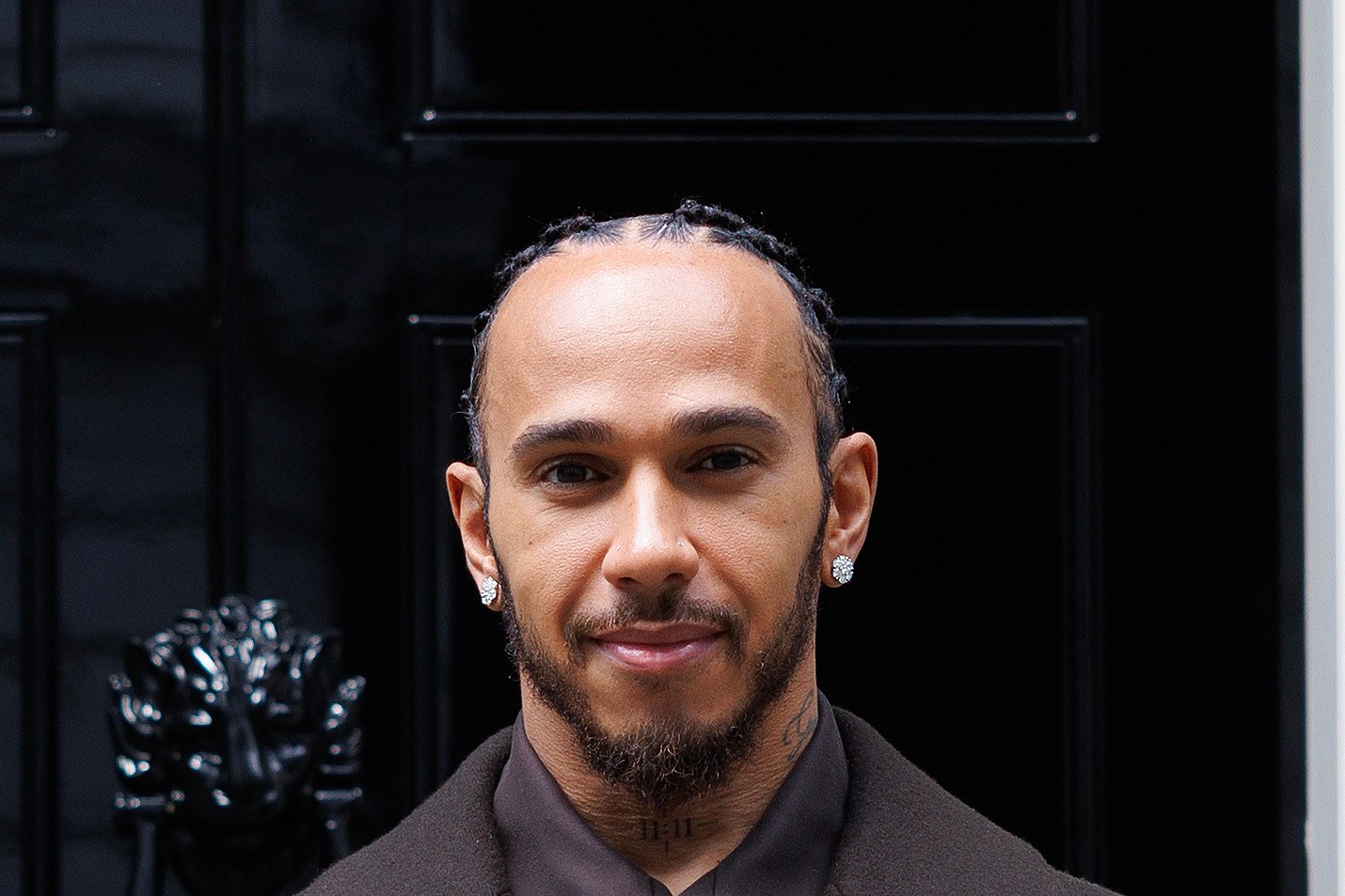 Lewis Hamilton smiling in a dark coat, outdoors