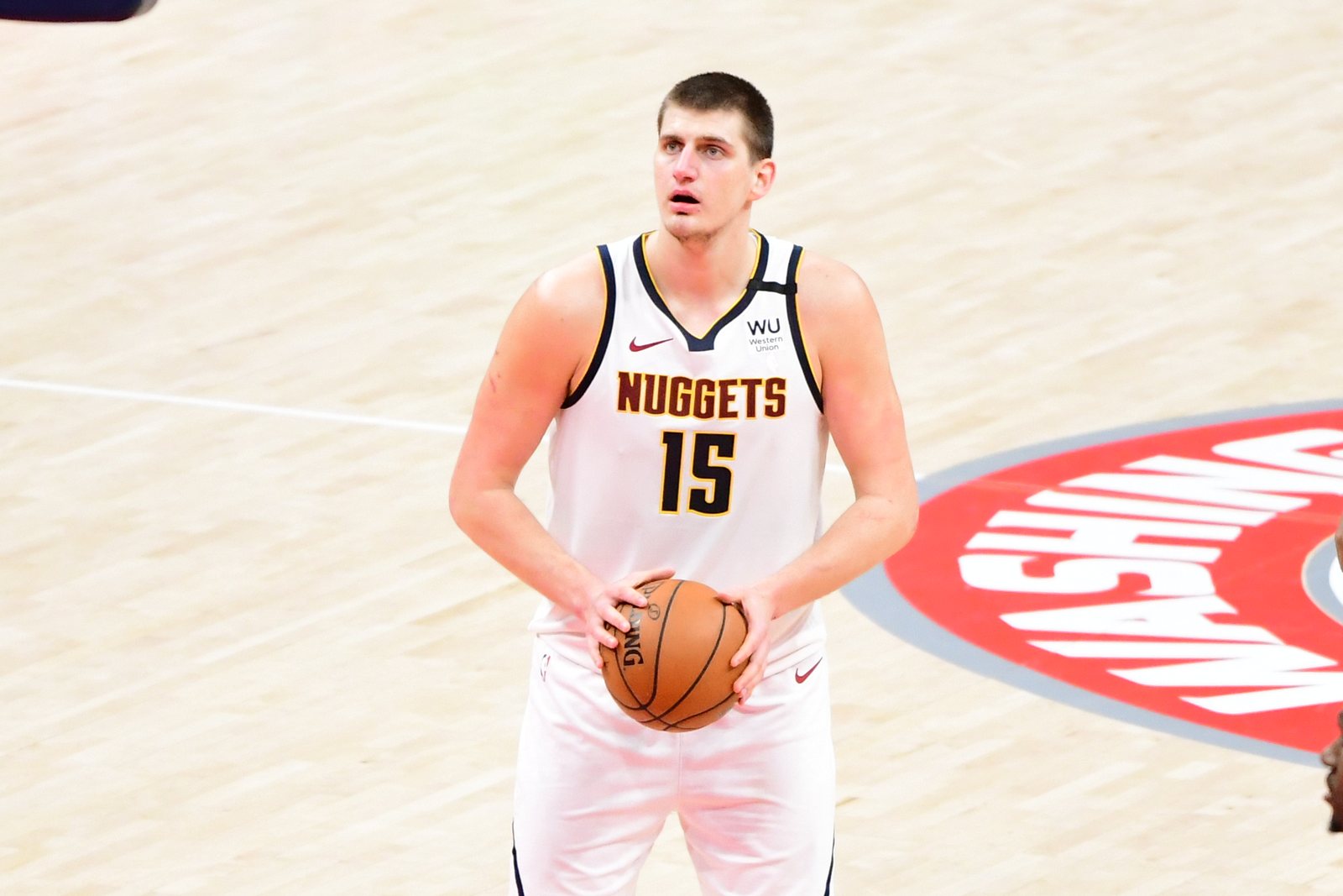Nikola Jokic in a white Denver Nuggets jersey, number 15, holds the ball at the free-throw line